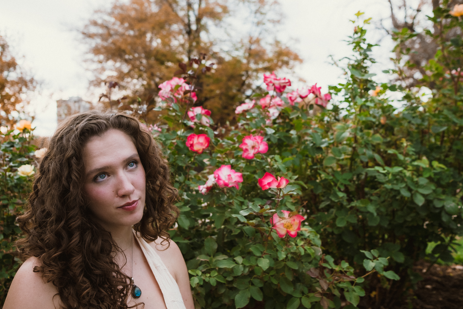 Emily posing by pink roses in an autumn garden